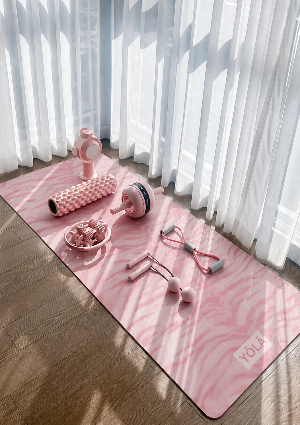Soft pink zebra-print YOLA yoga mat styled in a sunlit minimalist home gym setup with pink fitness accessories, sheer white curtains, warm wooden floors, and natural shadows creating a calm aesthetic wellness vibe.