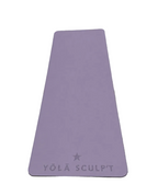 A lavender purple yoga mat with the brand name 'YŌLĀ SCULPT' and a star logo printed at the bottom, laid flat on a gray textured carpet.