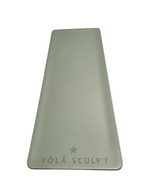 A rectangular yoga mat in a muted sage green color, featuring the brand name 'YŌLĀ SCULPT' and a star logo printed near the bottom, laid flat on a textured gray surface.