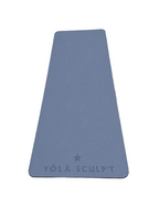 A slate blue yoga mat with the brand name 'YŌLÃ SCULPT' and a star logo printed at the bottom, laid flat on a gray textured surface.