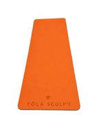 An orange yoga mat with the brand name 'YŌLĀ SCULPT' and a star logo embossed at the bottom, laid flat on a gray textured surface.