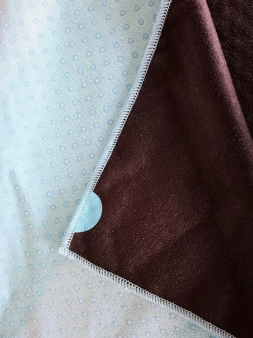 Close-up of hot dots yoga mat towel showing microfiber surface and non-slip silicone grip backing with stitched edge detail by Yola